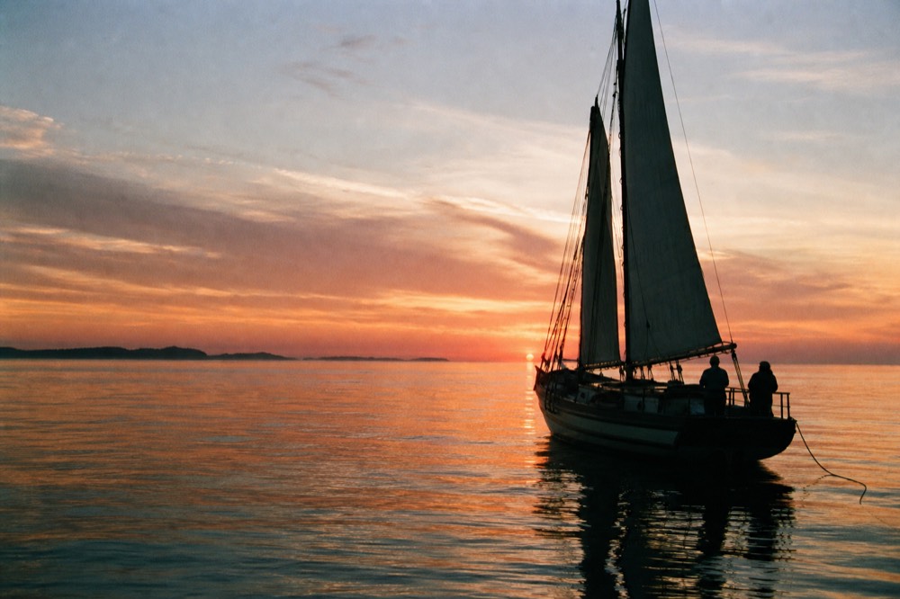 Schooner silhouetted against a vivid sunset sky with calm water, no text, no logos, no people