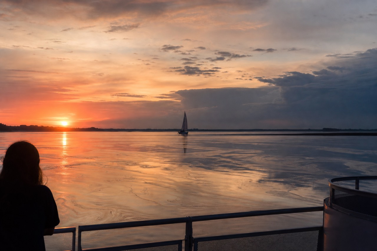 Sunset over calm Key West water with a sailboat silhouette, no text, no logos, no people