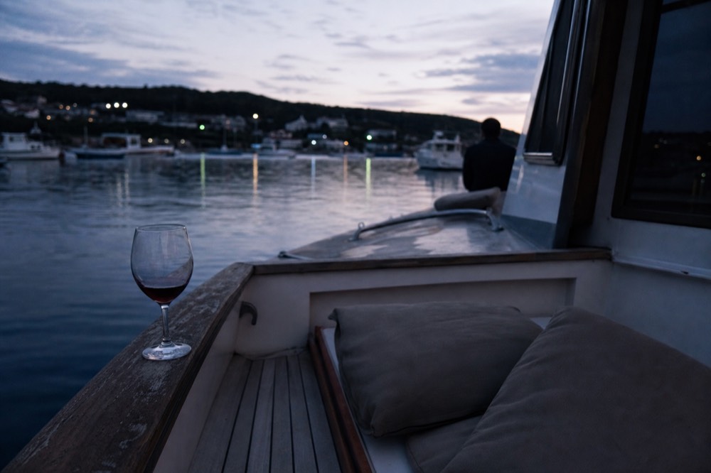 An empty deck of a boat at dusk with a glass of wine resting on a rail, no text, no logos, no people