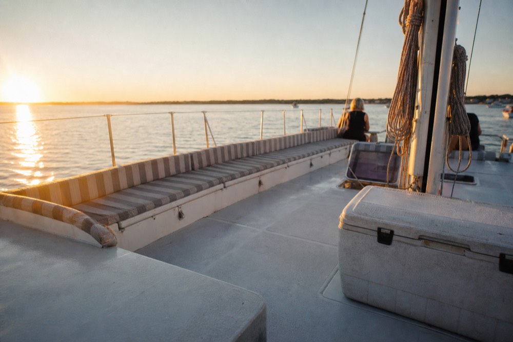 Open deck of a catamaran at golden hour with cushions and railings, no text, no logos, no people