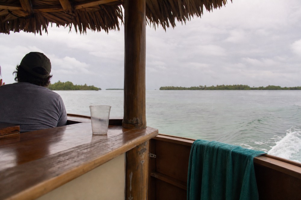 Open tiki-style boat with thatched bar canopy heading out on calm water, no text, no logos, no people
