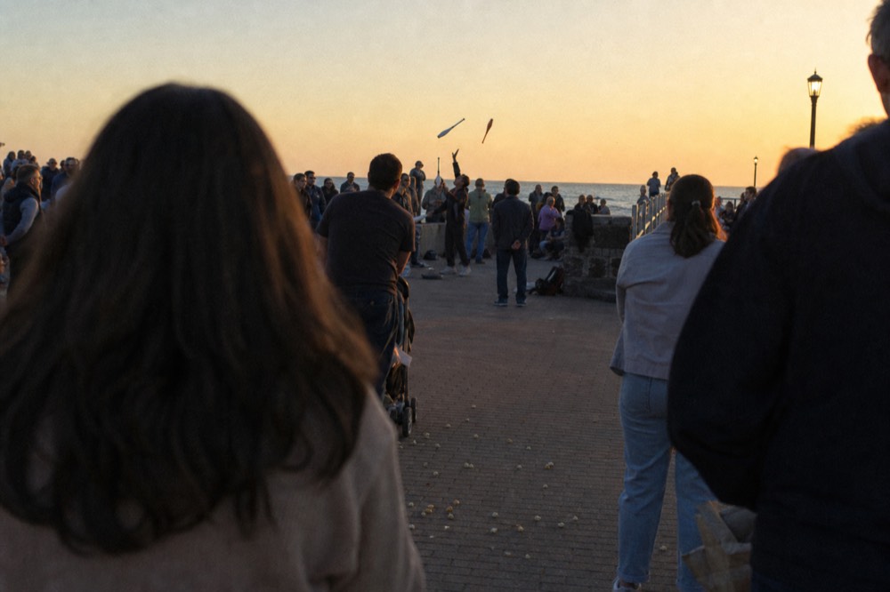 Crowds gathered along a waterfront boardwalk watching street performers before sunset, no text, no logos, no people