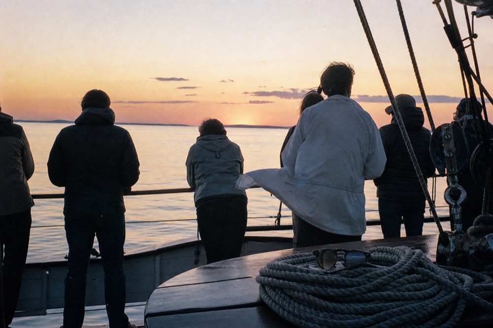 Passengers standing at the rail of a schooner as the sun sets over calm Gulf water, no text, no logos, no people