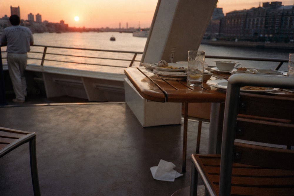 A table set with plates and drinks on the deck of a boat at sunset, no text, no logos, no people