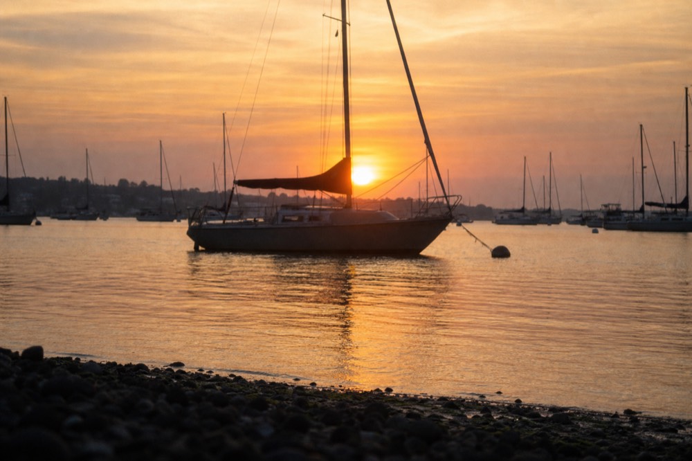The sun setting behind a silhouetted sailboat on calm water near Key West, no text, no logos, no people