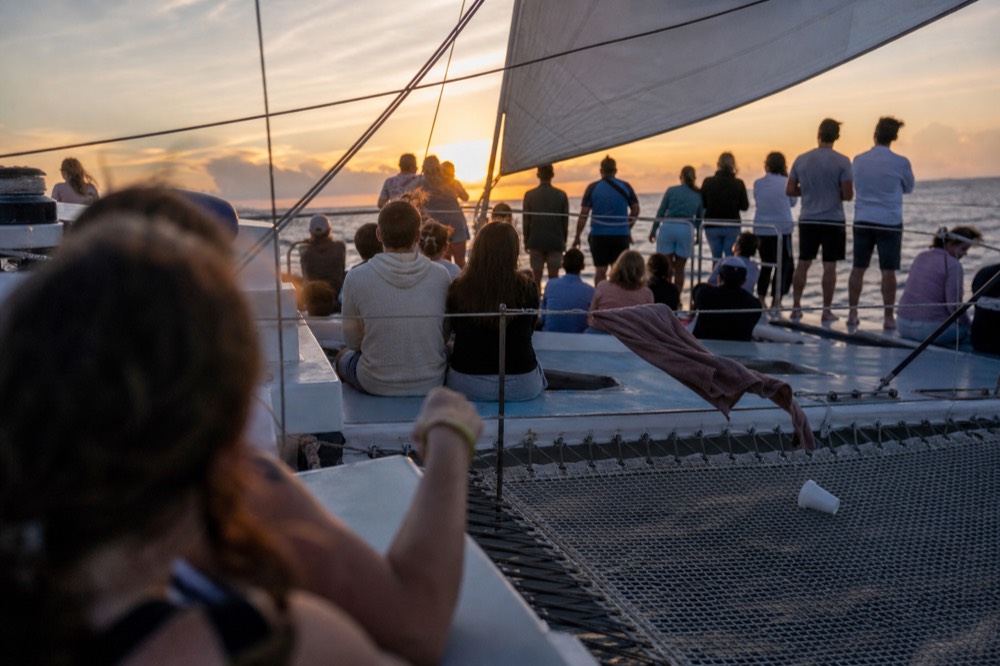 A wide catamaran deck crowded with passengers under sail at sunset off Key West, no text, no logos, no people