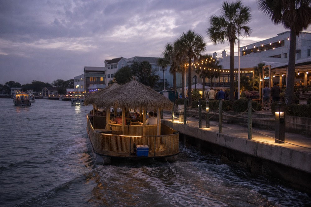 A tiki-style boat cruising near Key West at dusk with string lights glowing, no text, no logos, no people