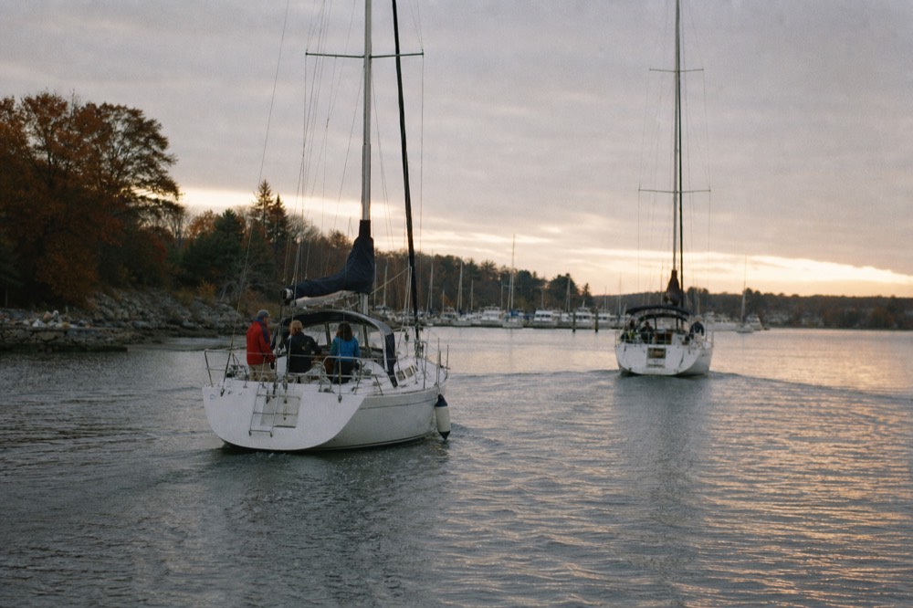 A sunset over calm water with sailboats returning to a marina, no text, no logos, no people