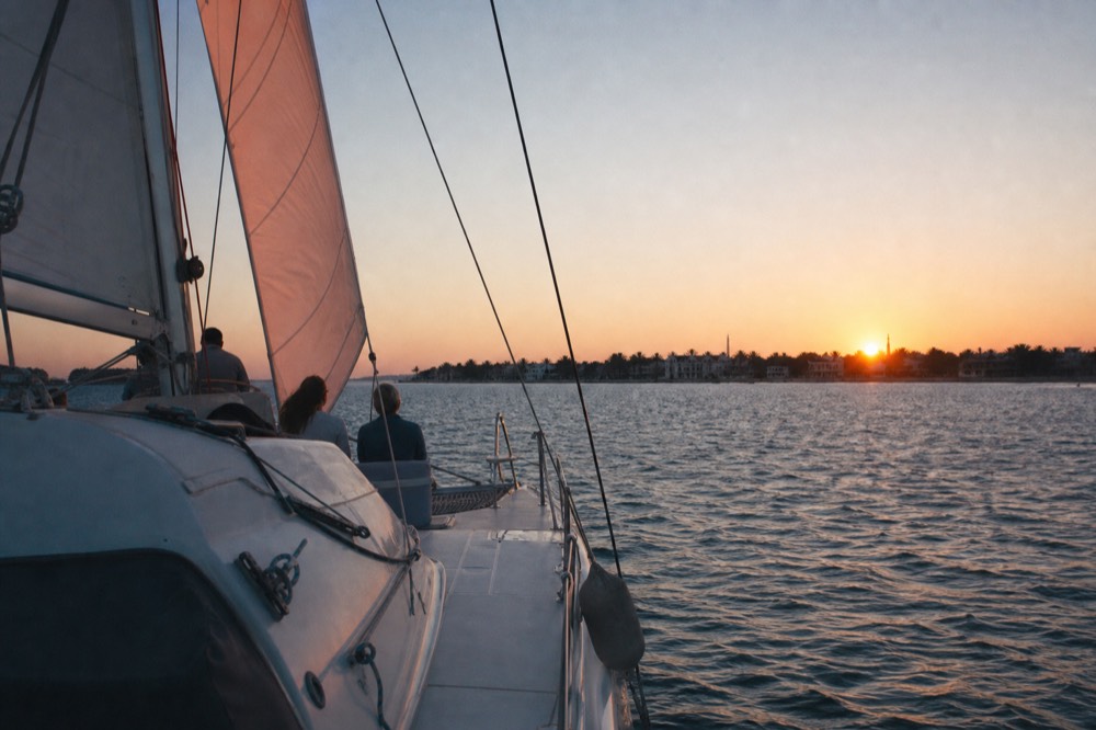 A catamaran under sail on calm water as the sun sets behind Key West, no text, no logos, no people.