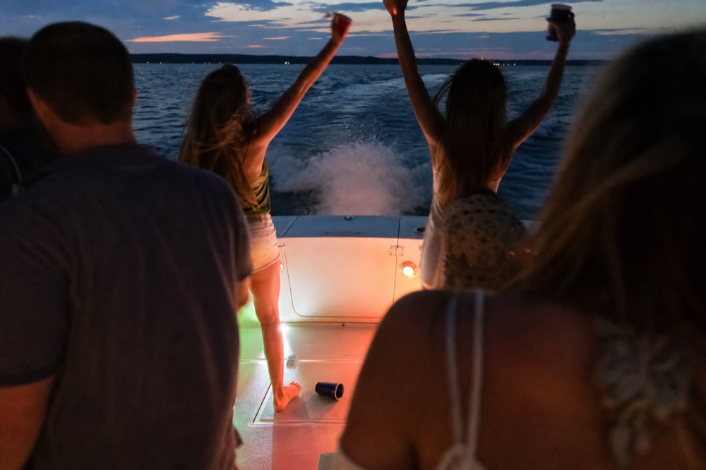 Passengers gathered around the stern of a boat at dusk with drinks raised, no text, no logos, no people