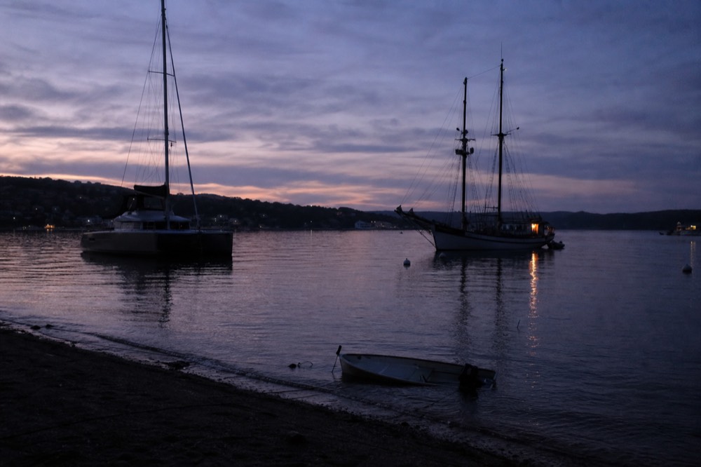 A catamaran and a tall ship at anchor in a harbor at dusk, no text, no logos, no people.