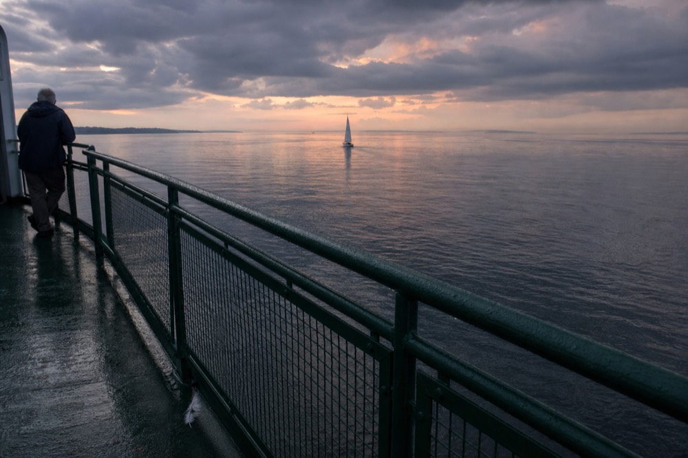 Clouds breaking over calm sea at dusk with a distant sailboat, no text, no logos, no people
