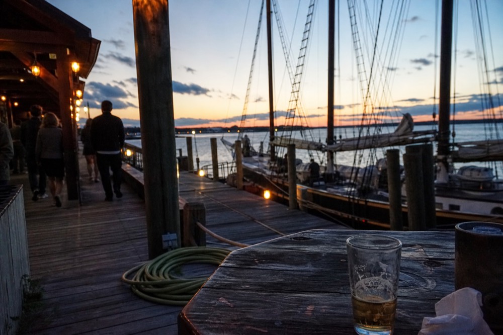 A historic seaport dock at dusk with masts and warm lights, no text, no logos, no people